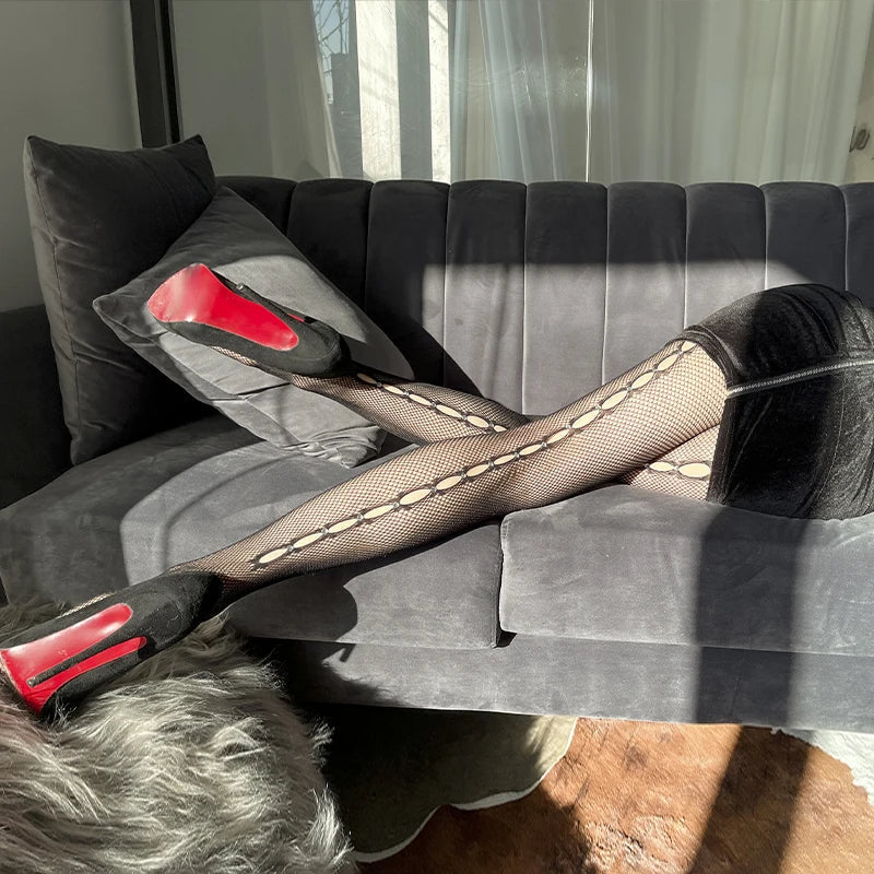 Pair of fishnet stockings with red-soled high heels on a gray couch.