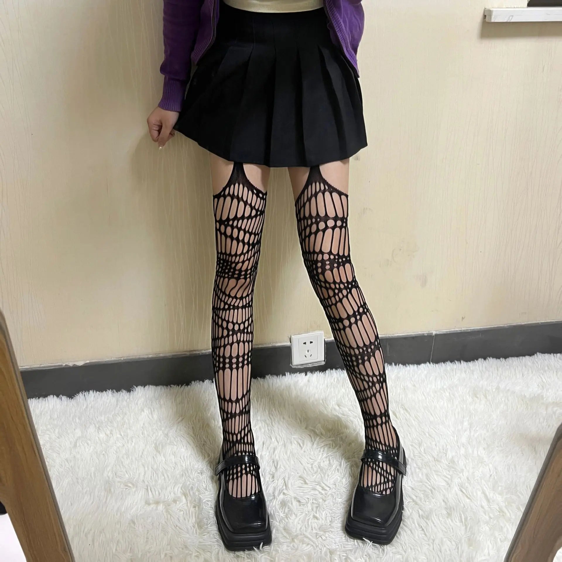 Pair of black patterned fishnet stockings worn with a short skirt and chunky shoes.