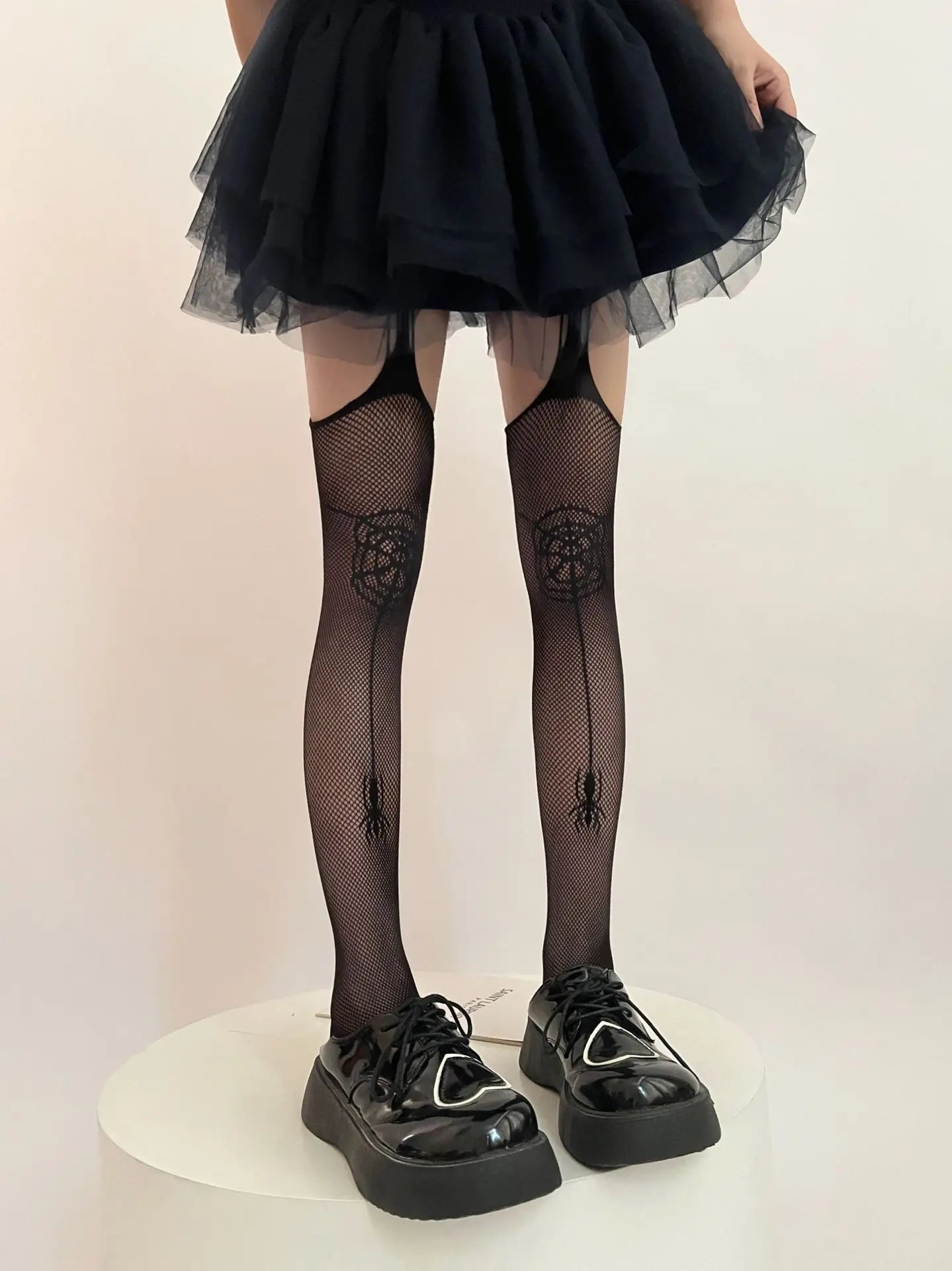 Black fishnet stockings with spider web and spider designs, worn with a tulle skirt and chunky platform shoes.